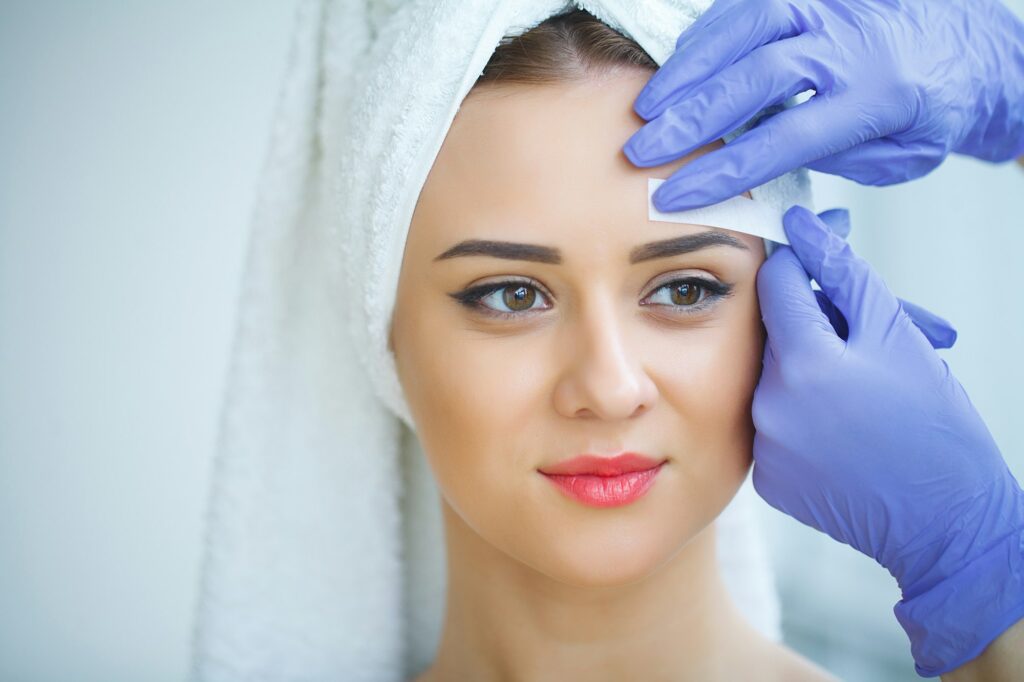 Beautician waxing young woman's eyebrows in spa center